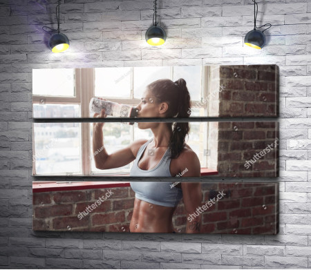 Девушка со спортивной фигурой пьет воду в фитнес зале