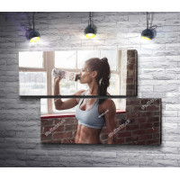 Девушка со спортивной фигурой пьет воду в фитнес зале